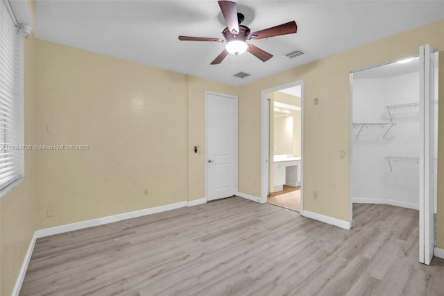 unfurnished bedroom featuring a walk in closet, ensuite bath, light hardwood / wood-style flooring, ceiling fan, and a closet