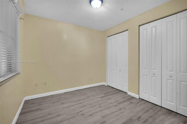 unfurnished bedroom featuring a textured ceiling, two closets, and light wood-type flooring