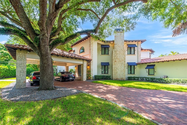 mediterranean / spanish house with a tile roof, a chimney, decorative driveway, a front yard, and stucco siding