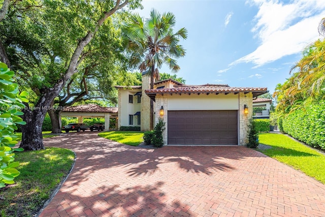 mediterranean / spanish house with stucco siding, stone siding, decorative driveway, a tiled roof, and an attached garage