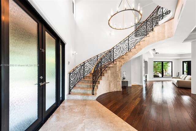 entrance foyer with wood-type flooring, a towering ceiling, french doors, and crown molding