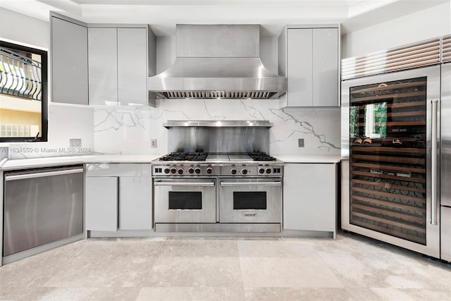 kitchen with gray cabinets, appliances with stainless steel finishes, tasteful backsplash, and wall chimney range hood