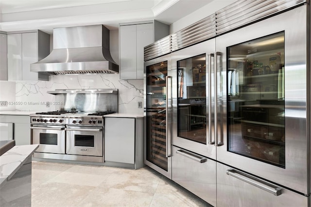 kitchen with gray cabinets, wall chimney exhaust hood, high end appliances, and decorative backsplash