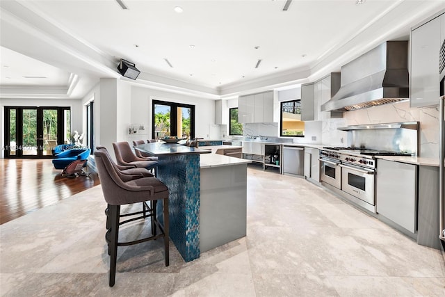 kitchen featuring a healthy amount of sunlight, wall chimney exhaust hood, a tray ceiling, and french doors