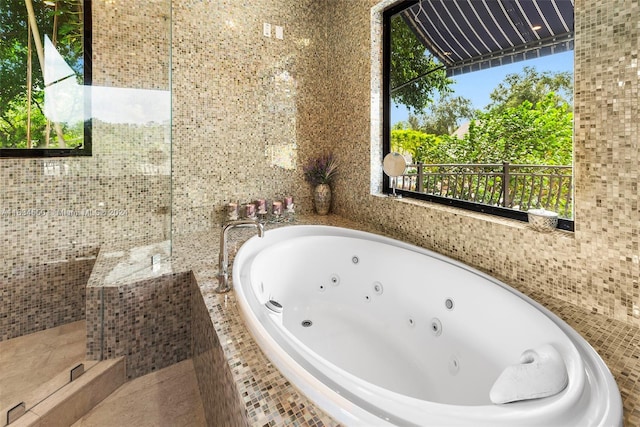 bathroom with a tub with jets and tile walls