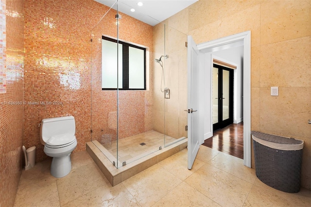 bathroom with tile walls, toilet, french doors, and an enclosed shower