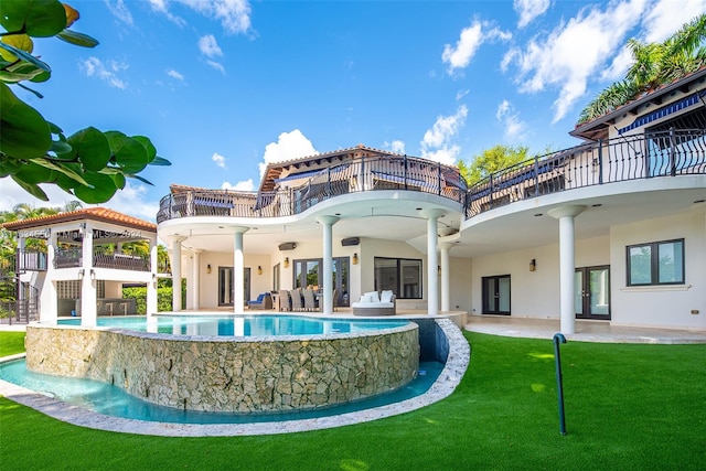 rear view of property featuring ceiling fan, a balcony, a lawn, and a patio area