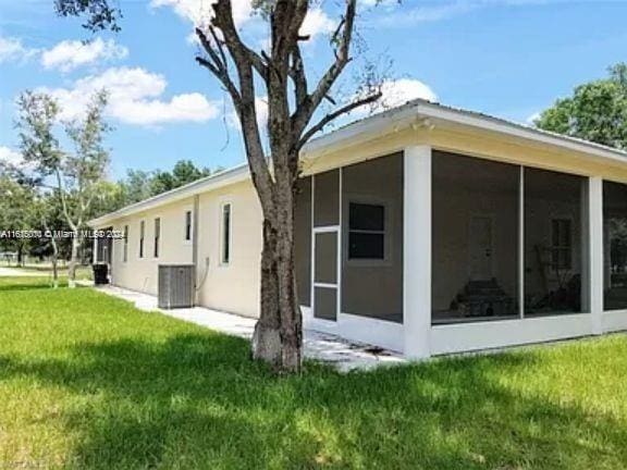 view of side of property with a sunroom, a lawn, and cooling unit