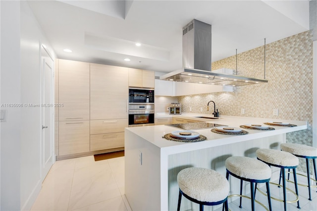 kitchen with kitchen peninsula, a breakfast bar, island range hood, sink, and black appliances