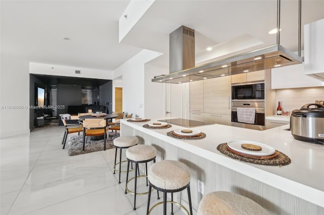 kitchen with backsplash, black appliances, a kitchen bar, kitchen peninsula, and island exhaust hood