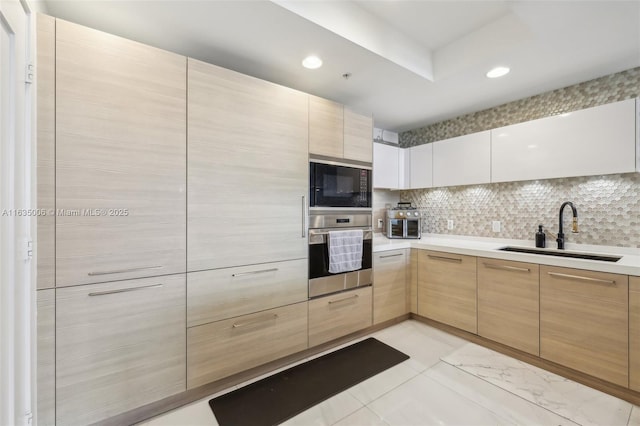 kitchen featuring black microwave, stainless steel oven, sink, backsplash, and light brown cabinetry