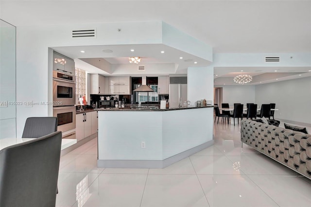 kitchen featuring dark stone countertops, light tile patterned floors, a tray ceiling, and stainless steel appliances