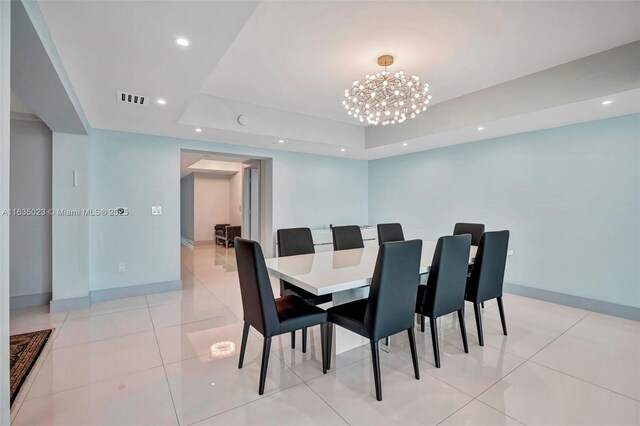 tiled dining space with an inviting chandelier and a tray ceiling