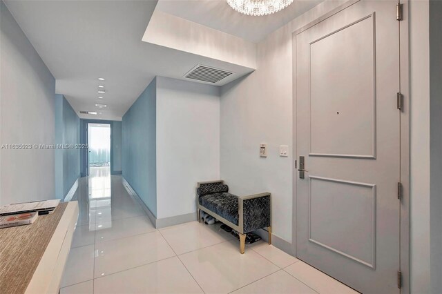 hall featuring baseboards, visible vents, tile patterned flooring, and an inviting chandelier