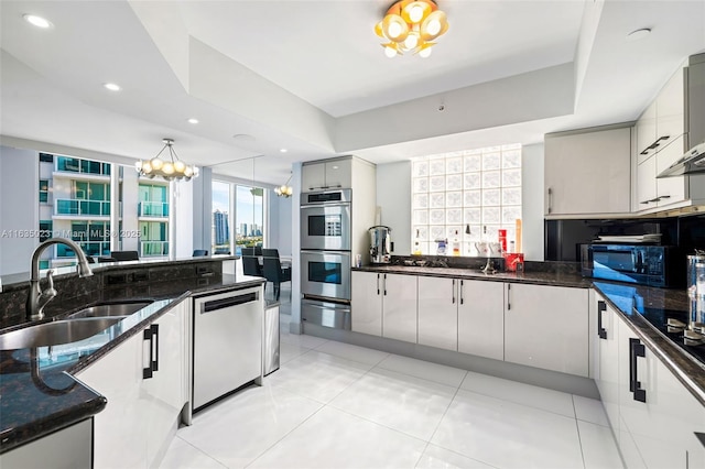 kitchen featuring pendant lighting, black appliances, sink, dark stone counters, and a tray ceiling