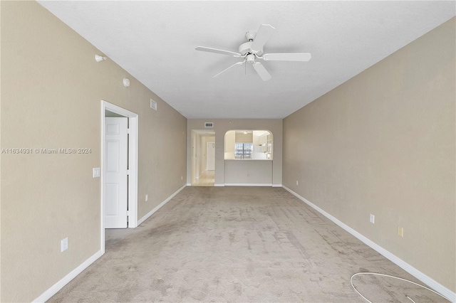 unfurnished room featuring arched walkways, light colored carpet, visible vents, baseboards, and a ceiling fan