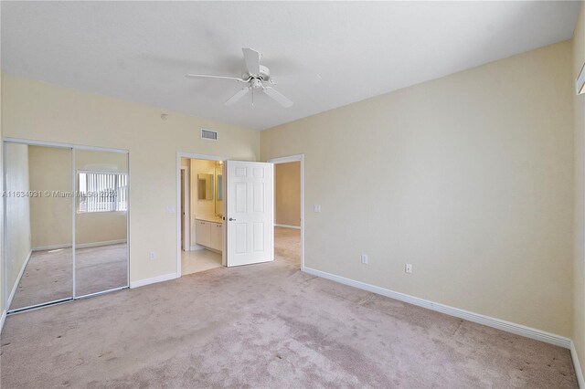 unfurnished bedroom featuring light carpet, ensuite bathroom, a closet, and ceiling fan