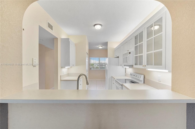 kitchen with a textured ceiling, white appliances, sink, and kitchen peninsula