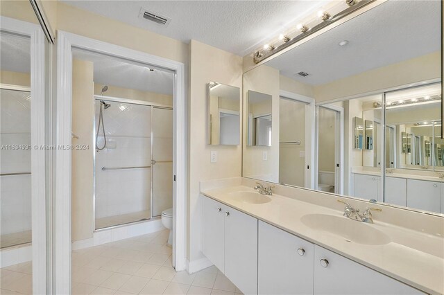 bathroom with a shower with shower door, tile patterned flooring, a textured ceiling, toilet, and double sink vanity