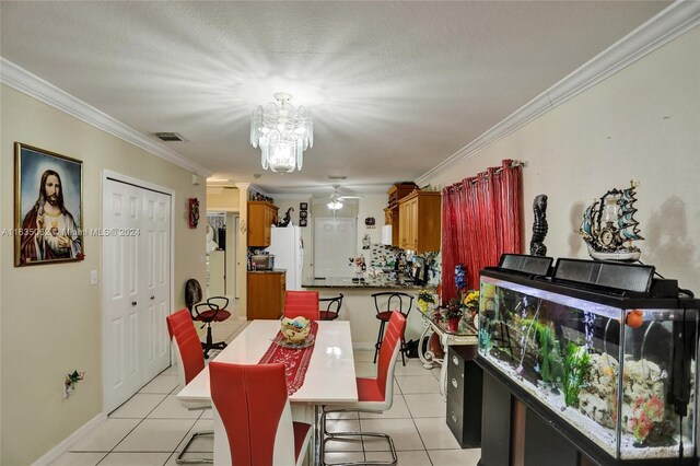 tiled dining room featuring a textured ceiling, ornamental molding, and ceiling fan with notable chandelier