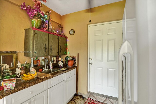 kitchen featuring dark stone counters, white cabinets, light tile patterned floors, and sink