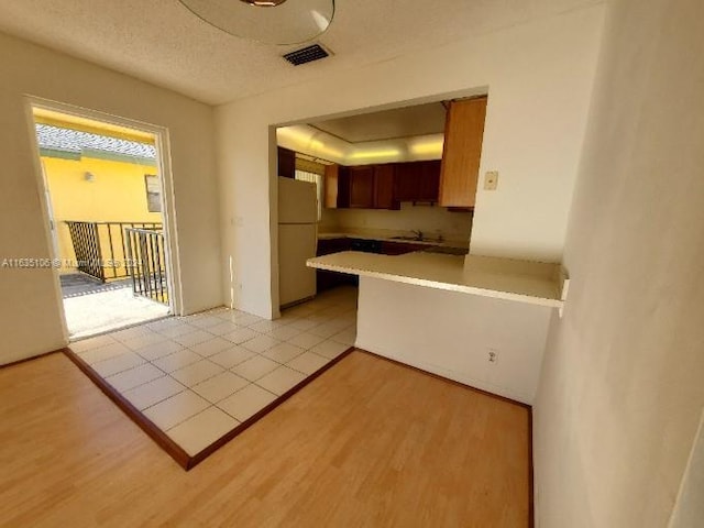 kitchen with sink, white refrigerator, kitchen peninsula, a textured ceiling, and light hardwood / wood-style flooring