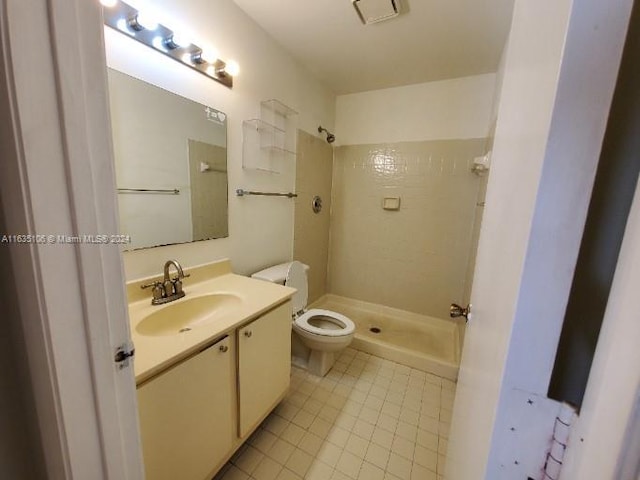 bathroom with a tile shower, vanity, tile patterned flooring, and toilet