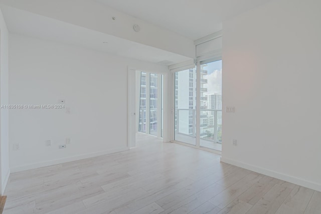 spare room with a wall of windows and light hardwood / wood-style flooring