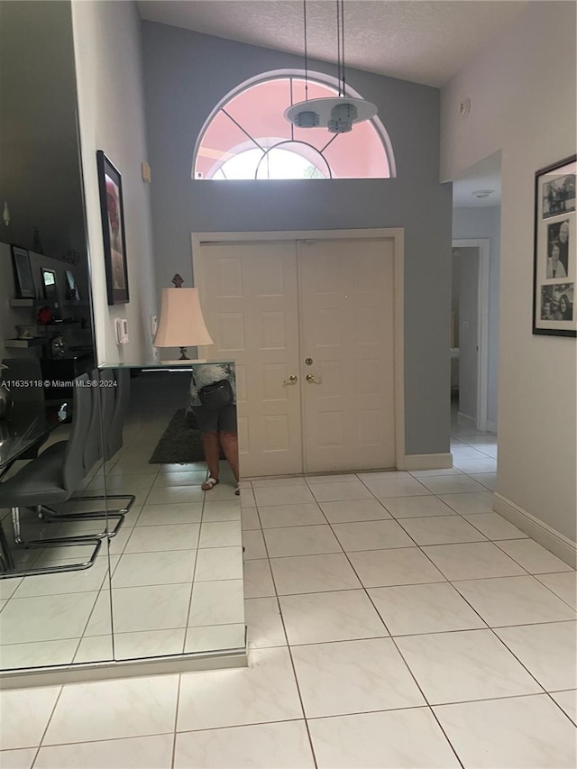 foyer with light tile patterned floors, high vaulted ceiling, a textured ceiling, and baseboards