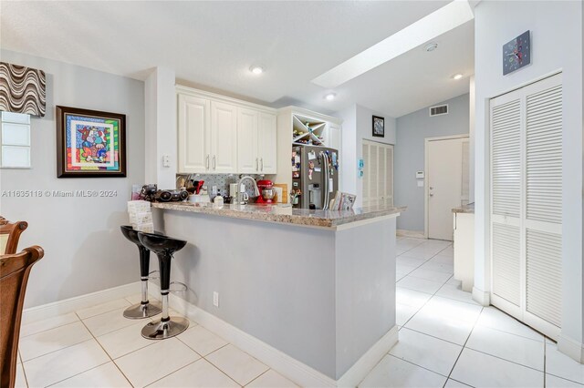 kitchen with white cabinetry, kitchen peninsula, stainless steel fridge, light tile patterned flooring, and tasteful backsplash