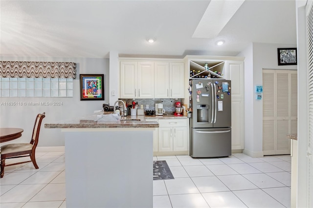 kitchen with light tile patterned floors, a peninsula, a sink, stainless steel refrigerator with ice dispenser, and tasteful backsplash