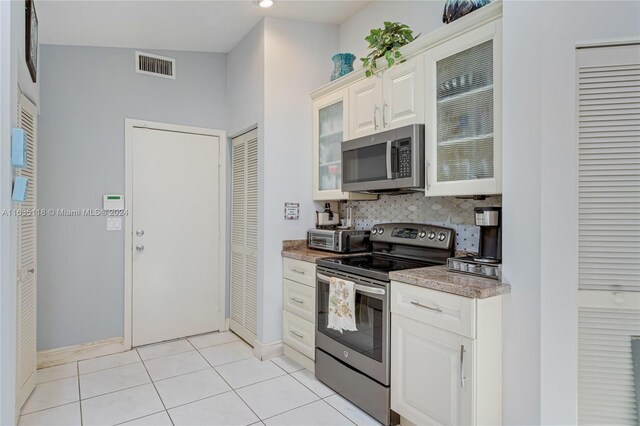 kitchen featuring decorative backsplash, appliances with stainless steel finishes, white cabinets, light tile patterned flooring, and vaulted ceiling