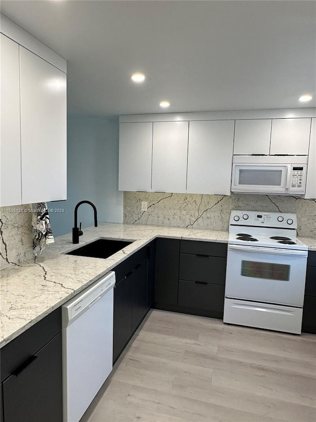 kitchen with light stone counters, white appliances, sink, and light hardwood / wood-style flooring