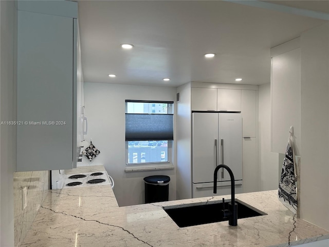 kitchen with white fridge, white cabinetry, sink, light stone counters, and stove