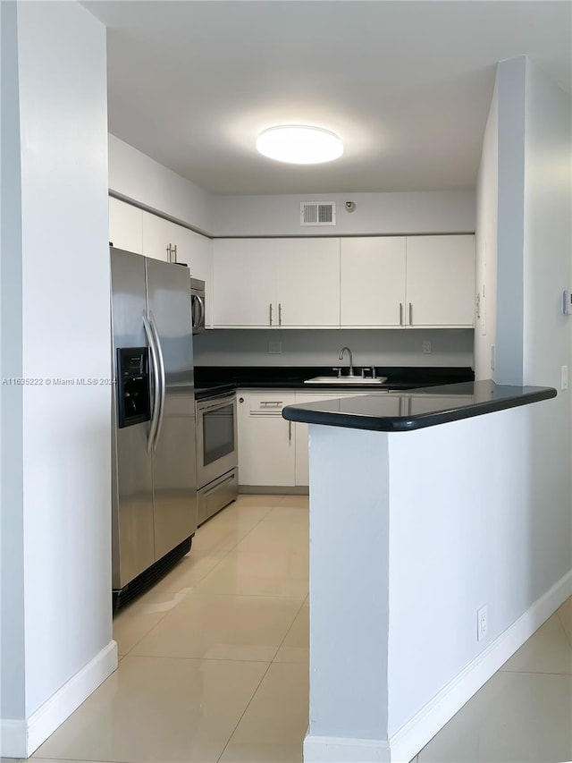 kitchen with light tile patterned floors, kitchen peninsula, white cabinets, stainless steel appliances, and sink