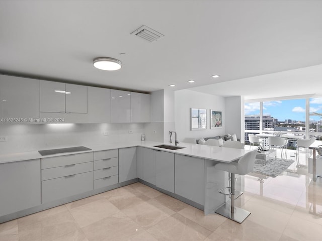 kitchen featuring light tile patterned flooring, kitchen peninsula, gray cabinets, a kitchen breakfast bar, and sink