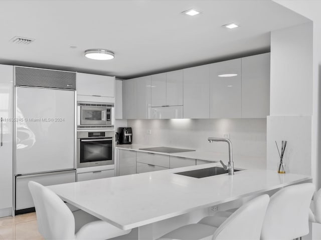 kitchen featuring light tile patterned flooring, built in appliances, sink, a breakfast bar area, and backsplash