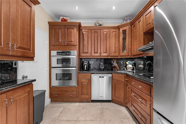 kitchen with light tile patterned flooring, crown molding, dark stone counters, backsplash, and appliances with stainless steel finishes