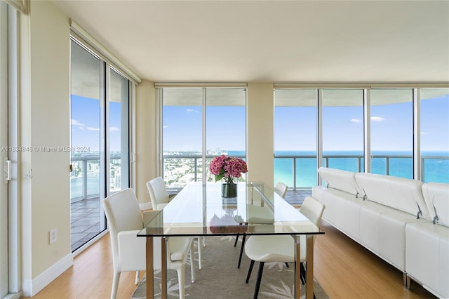 dining area with floor to ceiling windows, a water view, and light hardwood / wood-style floors