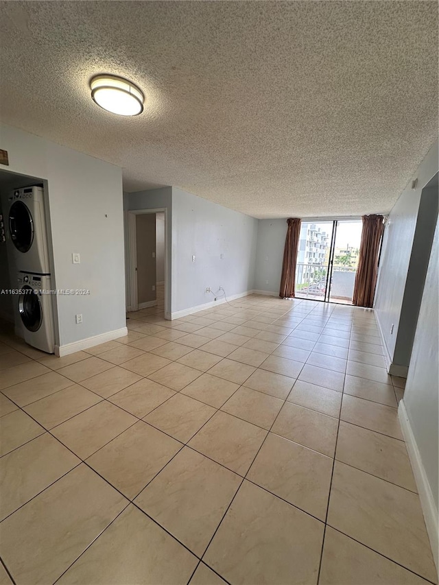 empty room featuring stacked washer / drying machine, light tile patterned floors, a wall of windows, and a textured ceiling