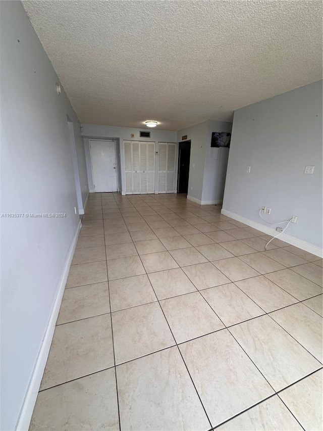 empty room with a textured ceiling and light tile patterned floors