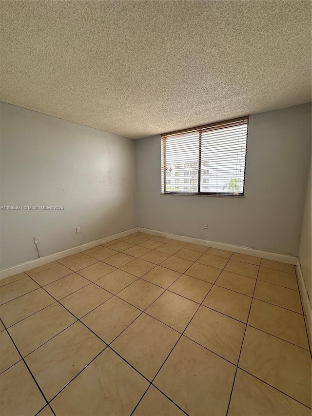 empty room with a textured ceiling, baseboards, and light tile patterned floors