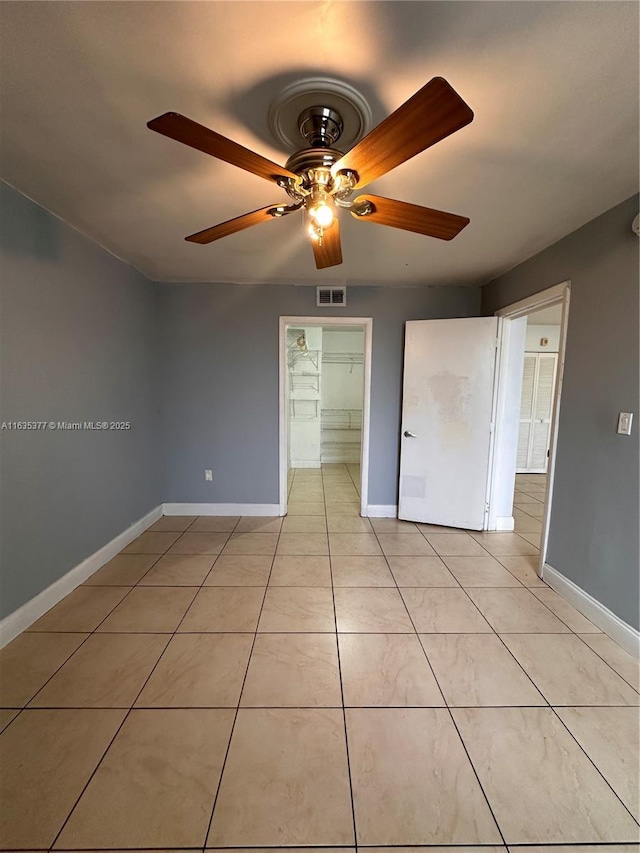 unfurnished bedroom with a walk in closet, a closet, ceiling fan, and light tile patterned flooring