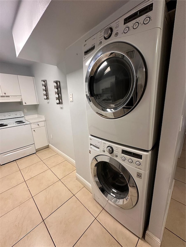 laundry area featuring light tile patterned floors, stacked washer and dryer, and baseboards