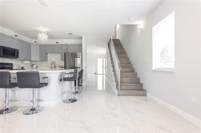 kitchen with tasteful backsplash, a breakfast bar area, light countertops, gray cabinets, and marble finish floor