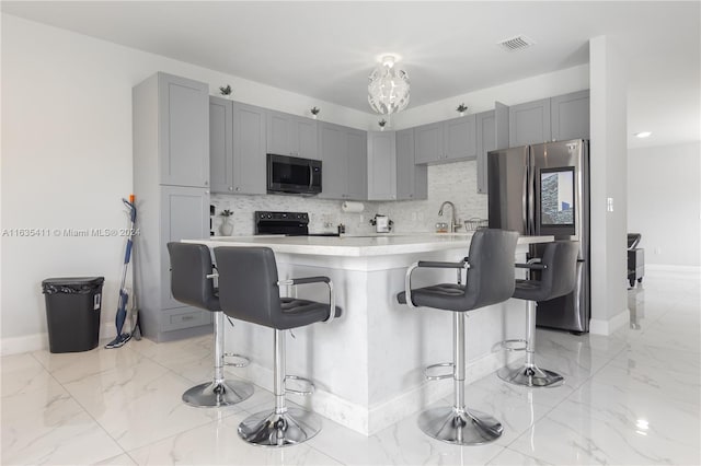 kitchen featuring gray cabinets, stainless steel appliances, light countertops, marble finish floor, and tasteful backsplash