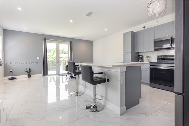 kitchen featuring marble finish floor, appliances with stainless steel finishes, a breakfast bar, and gray cabinetry