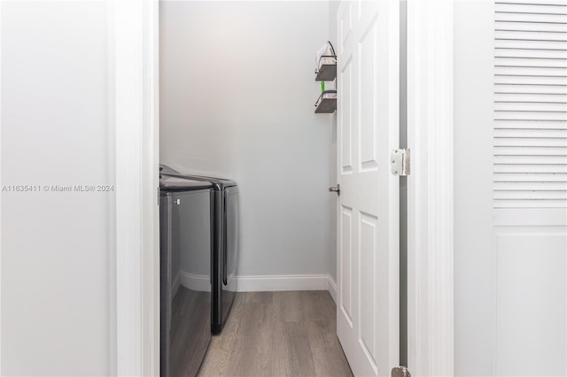 clothes washing area featuring laundry area, baseboards, light wood finished floors, and washer and clothes dryer