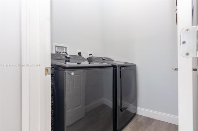 clothes washing area with baseboards, wood finished floors, laundry area, and washing machine and clothes dryer