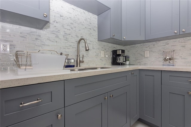 kitchen with tasteful backsplash, gray cabinetry, light stone counters, and a sink